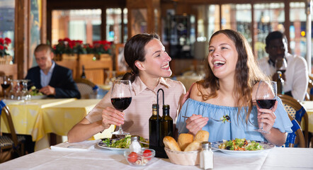 Two positive females dining in restaurant, enjoying meal and conversation