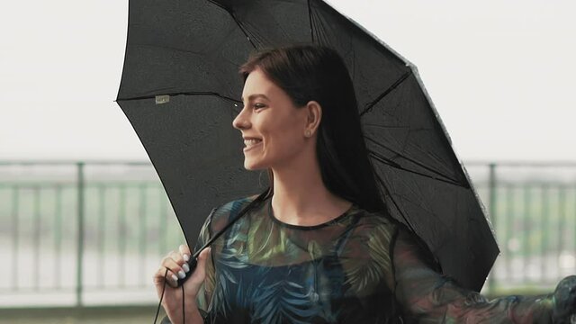 Smiling woman with black umbrella stands under light rain