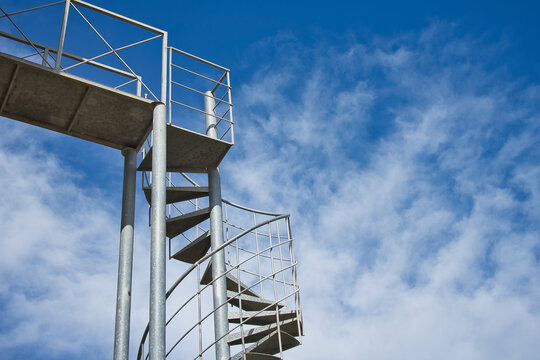 Metal spiral staircase on a blue sky background. Copy space. Text