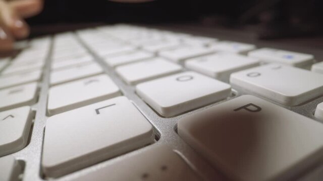 Woman hands type pressing white keys with letters on contemporary computer keyboard at table on black background extreme close view