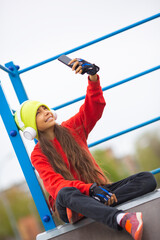 Obraz premium Vertical photo of a ten-year-old girl in white headphones takes a selfie on a smartphone to send to friends.