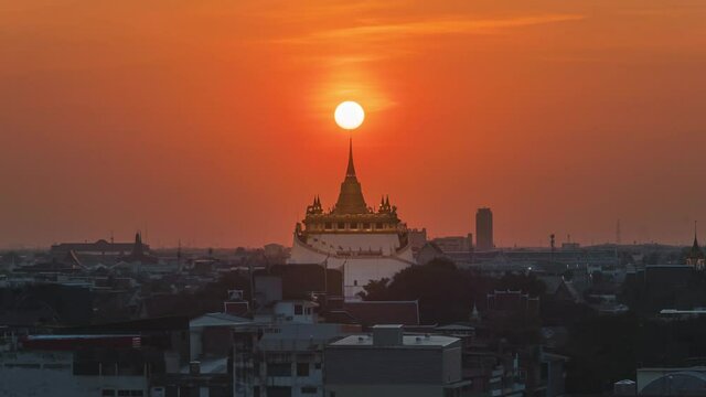 Time lapse Sunset in Bangkok city of Thailand on top of the pagoda Golden mountain, Wat Saket. The Sun falling on and piercing through pagoda's peak under the golden sky in the evening.