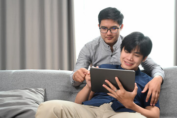 Happy of homosexual couple embracing and using digital tablet together in living room. Homosexual, LGBT concept.