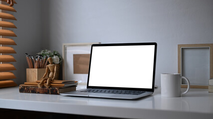 Computer laptop with blank screen, houseplant, pencil holder and coffee cup on white desk near window.