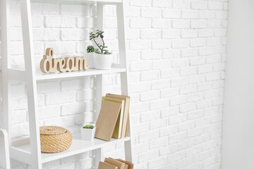 Shelf unit with books and decor near light brick wall