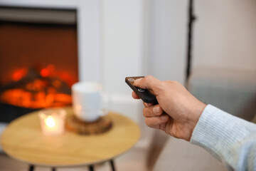 Young man adjusting electric fireplace at home