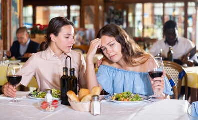 Two young female friends depressed at dinner in a restaurant, worrying about something