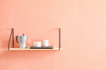 Shelf with coffee maker and cups hanging on color wall