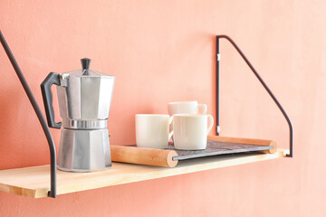 Shelf with coffee maker and cups hanging on color wall