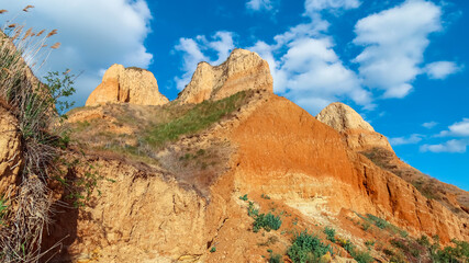 Fototapeta premium Landscape view clay cape cliffs. Green grass, lawns grown on slopes of clay mountains against blue sky. Hills of mountain and slopes of cape are overgrown with half grass and plants. Long web banner