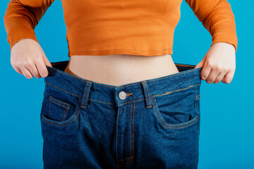 Skinny weight loss woman show flat stomach pulling by hands oversized big blue pants jeans. Slim...