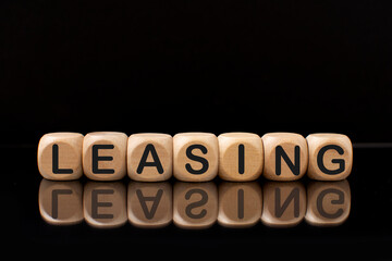 Wooden blocks with the word Leasing with a reflection on a black background .