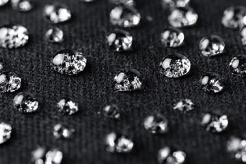 Water drops on waterproof black fabric close-up. Water resistant textile. 