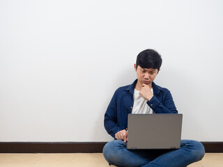 Man sit on the floor using laptop and feeling serious and hesitate on white wall