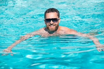 Man at summer vacation. Guy in sunglasses relaxing in swimming pool. Summertime pool resort.