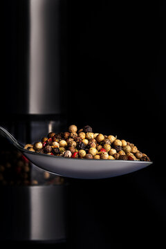Pepper peas in a tablespoon on the background of peppercorns