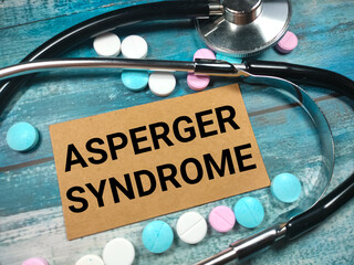 Text ASPERGER SYNDROME on a wooden blue background near a stethoscope and pills. Medical concept.