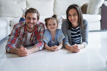 Young caucasian family with small daughter pose relax on floor in living room, smiling little girl kid hug embrace parents, show love and gratitude, rest at home together.