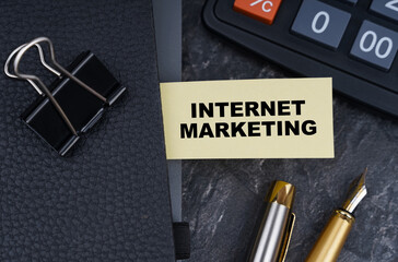 On the table is a calculator, a pen and a notebook with a bookmark on which it is written - Internet Marketing