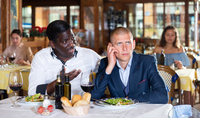 Man talking with upset friend during dinner at restaurant