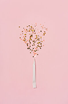 Explosion of sparkles from hahd rolled paper cigarette, on pastel pink background. flat lay