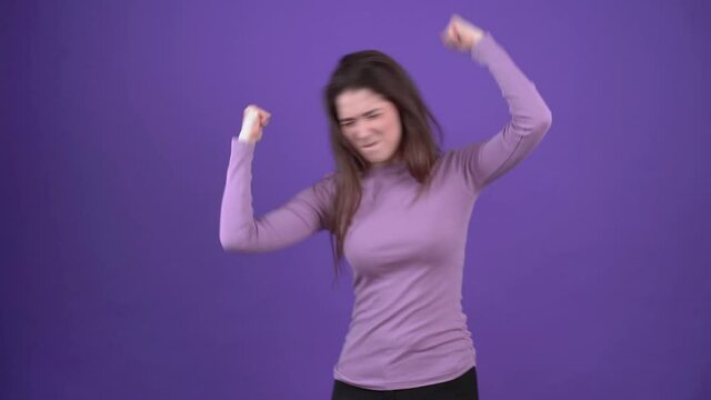 Let's Dance. The carefree girl dances charismatically under hip hop music. Brunette isolated on a purple background, dressed in a purple sweater. Lifestyle concept