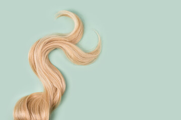 Curly blonde hair on mint background. Beautiful healthy long blond hair lock, haircut, hairstyle....