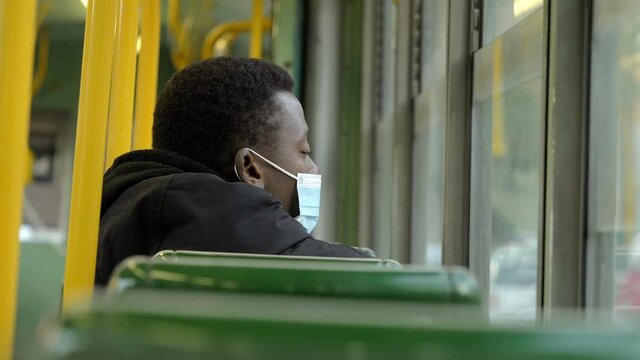 covid19 - young tired black man on the bus with mask looks out the window