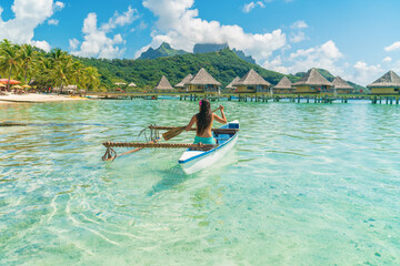 French Polynesia Tahiti travel vacation concept. Outrigger Canoe polynesian watersport sport woman paddling in traditional vaa boat. Water leisure activity, Bora Bora overwater bungalow resort hotel. - obrazy, fototapety, plakaty
