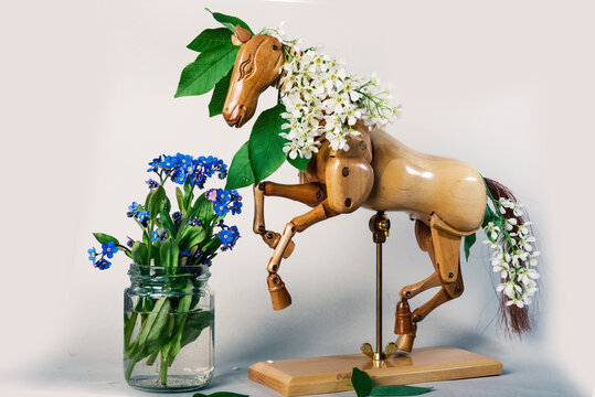 wooden articulated dummy horse mannequin in white inflorescences with a small bouquet of wild flowers in a small glass jar