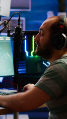 Competitive gamer with headphones using stream chat on powerful computer playing online shooter game late at night. Virtual online streaming cyber checking sound performing in gaming tournament