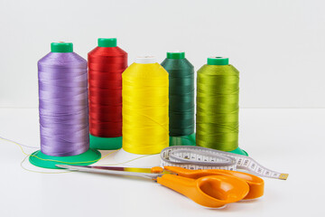 Colorful sewing threads, tailor's scissors and measuring tape in the foreground.