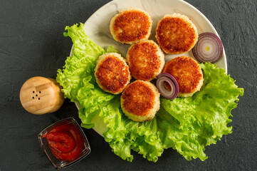 juicy delicious coated with breadcrumbs and fried chicken cutlets on white plate with spices and cetchup on dark background, view from above