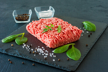 Raw minced beef meat on a slate with leaves and spices.