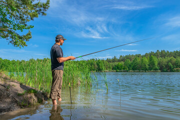 Fishing. Angler with float pole rod catch fish on on beautiful lake at green forest. Fisherman in action, man stand in water