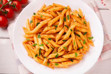 Penne pasta in tomato sauce, decorated with parsley on a white wooden table