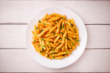Penne pasta in tomato sauce, decorated with parsley on a white wooden table