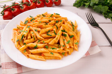 Penne pasta in tomato sauce, decorated with parsley on a white wooden table