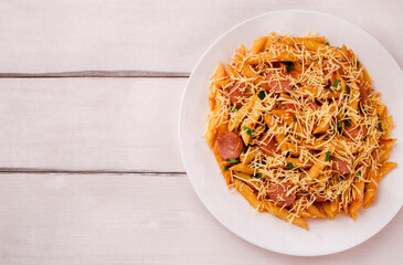 Penne pasta in tomato sauce with sausages and cheese, decorated with parsley on a white wooden table