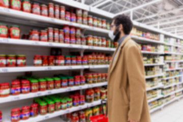A masked man in a supermarket selects goods on the shelves. Coronavirus pandemic. Blurred.