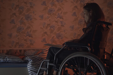 Young beautiful mother in a wheelchair reads a fairy tale to her child before bed. Disabled woman...