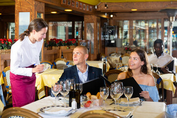 Diligent female waiter bringing order to visitors in restaurant. High quality photo