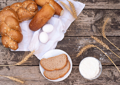 Fresh crispy bread and two eggs on white napkin with spikelets of wheat, bowl of flour, bread on plate on wooden table. Harvest season holiday World Bread Day. Bread is the staff of life. Top view.