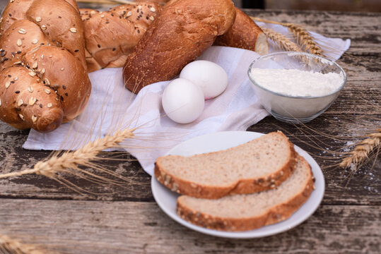 Fresh crispy bread and two eggs on white napkin with spikelets of wheat, bowl of flour, bread on plate on wooden table. Harvest season holiday World Bread Day. Bread is the staff of life. Side view.