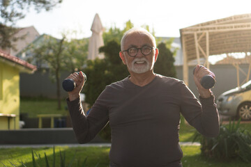 A good-looking, active senior man is exercising with the small barbells in the backyard.