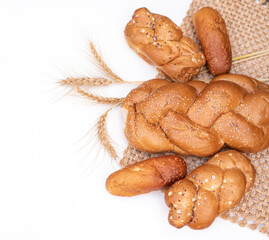 Fresh crispy bread  with spikelets of wheat on wicker napkin and white background. Harvest season holiday World Bread Day. Bread is the staff of life. Top view. Close-up.