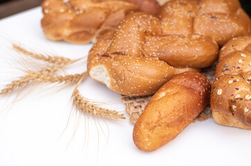 Fresh crispy bread  with spikelets of wheat on wicker napkin and white background table. Harvest season holiday World Bread Day. Bread is the staff of life. Side view. Close-up.