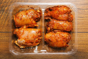 Raw uncooked Asian spice marinated chicken fillets in a plastic tray on a wooden table surface. Poultry product. Meat industry, Summer barbecue range. Meat in marinade with herb, oils and sauce.