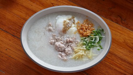 Asian congee with ground pork, egg and vegetable in a bowl on wooden background.