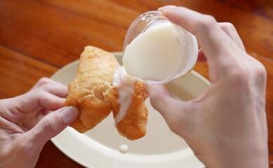 Hand hold deep fried dough or Patongkoh dipping  sweetened condensed milk.